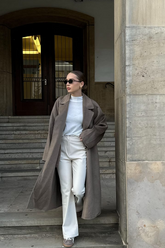 a lady in a white top, a pair of beige pants and a brown long wool coat